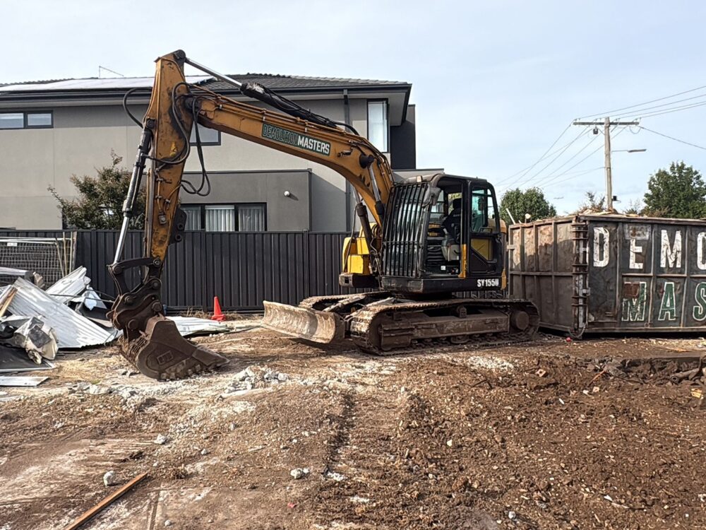Demolition Masters branded skip bin and yellow excavator on a residential demolition site