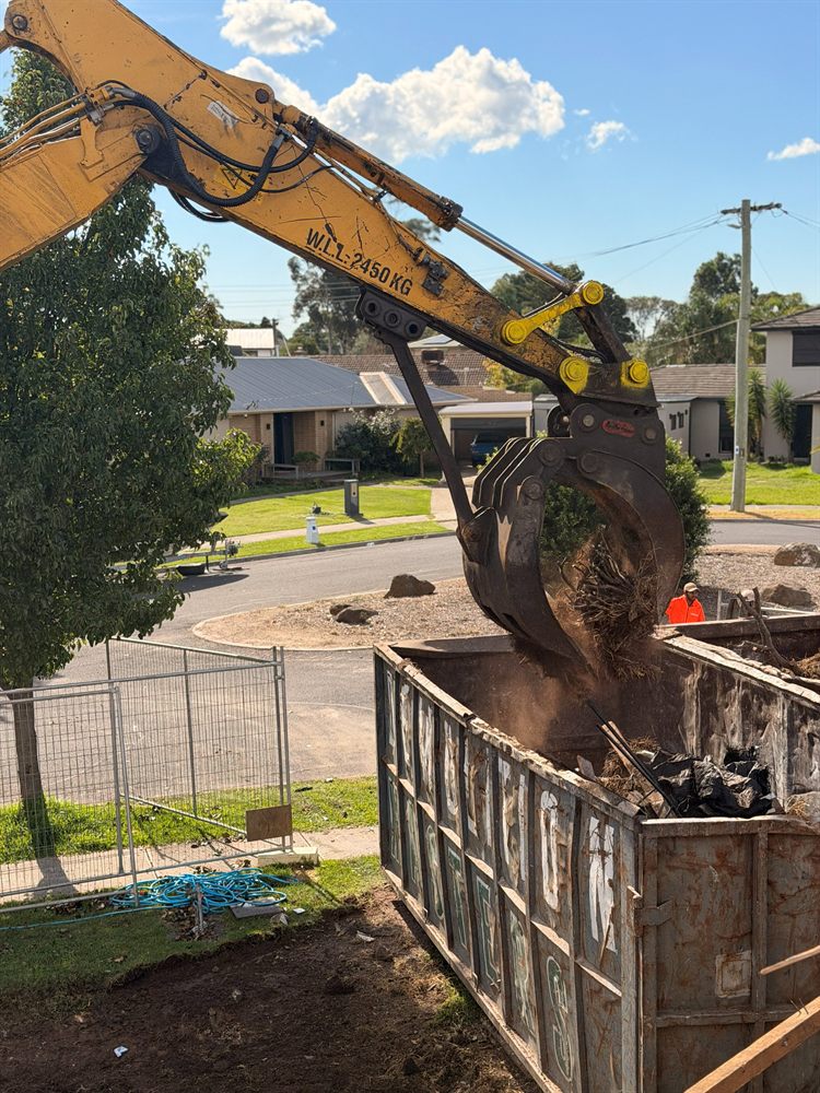 Excavator grab loading soil and demolition rubble into a Demolition Masters bin
