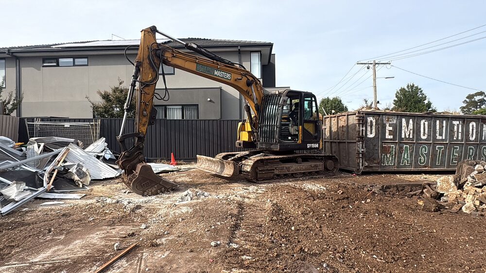 Excavator loading demolition debris into a Demolition Masters branded bin on a Melbourne site