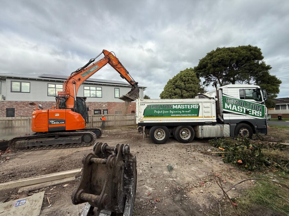 Branded Demolition Masters truck and excavator on site with a hi-vis crew member