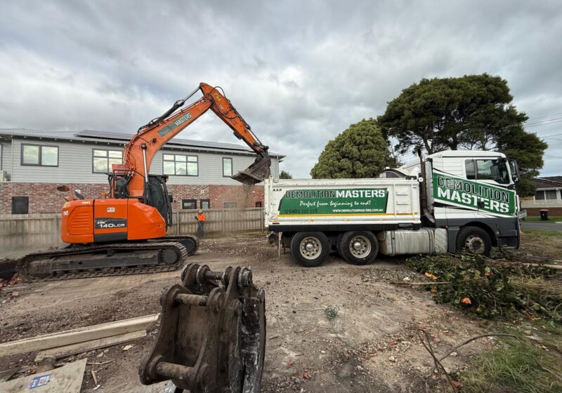 Branded Demolition Masters truck and excavator on site with a hi-vis crew member